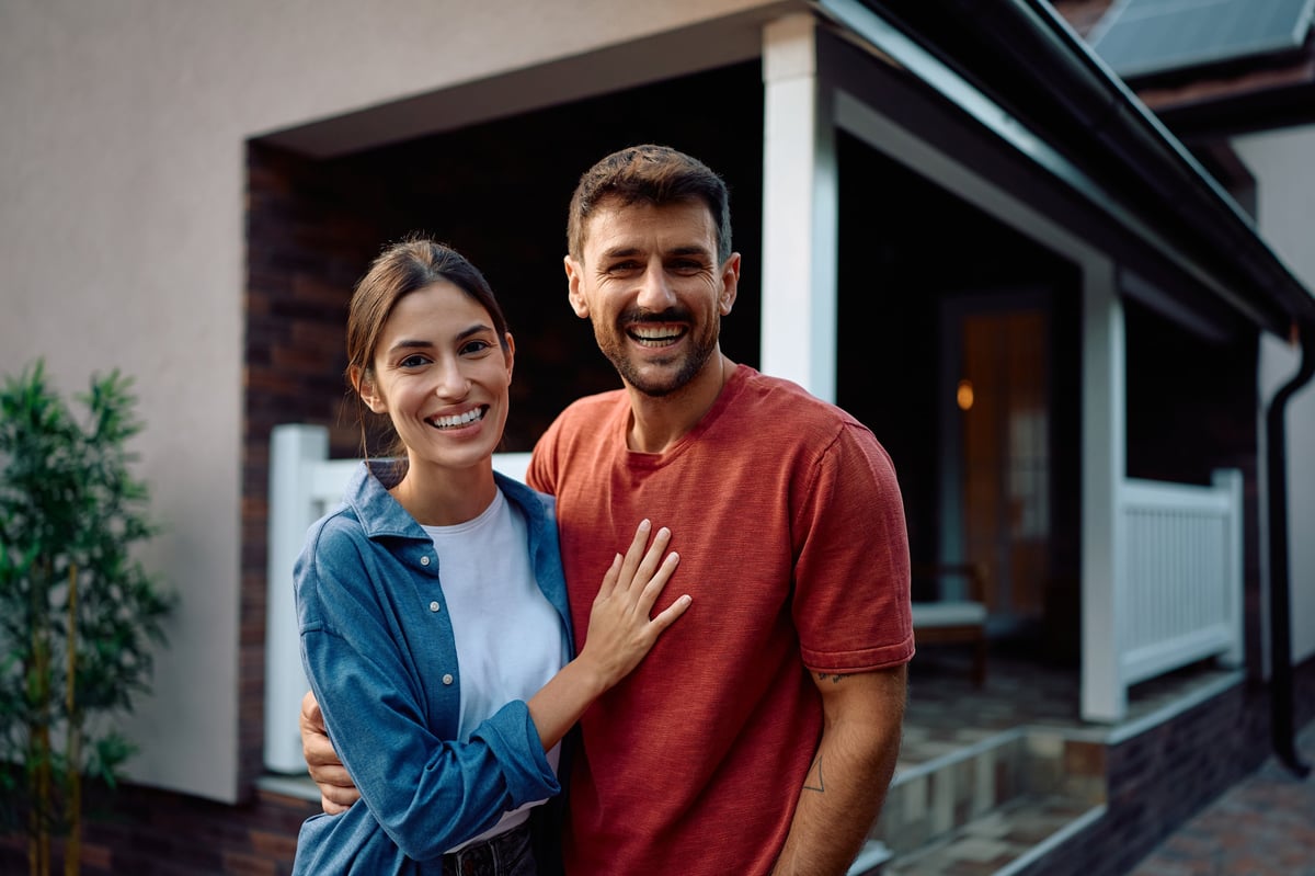 Happy couple proudly standing in front of their home